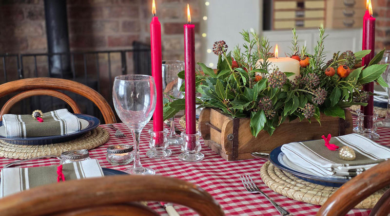 A festive christmas table with foliage centrepiece and red dinner candles.