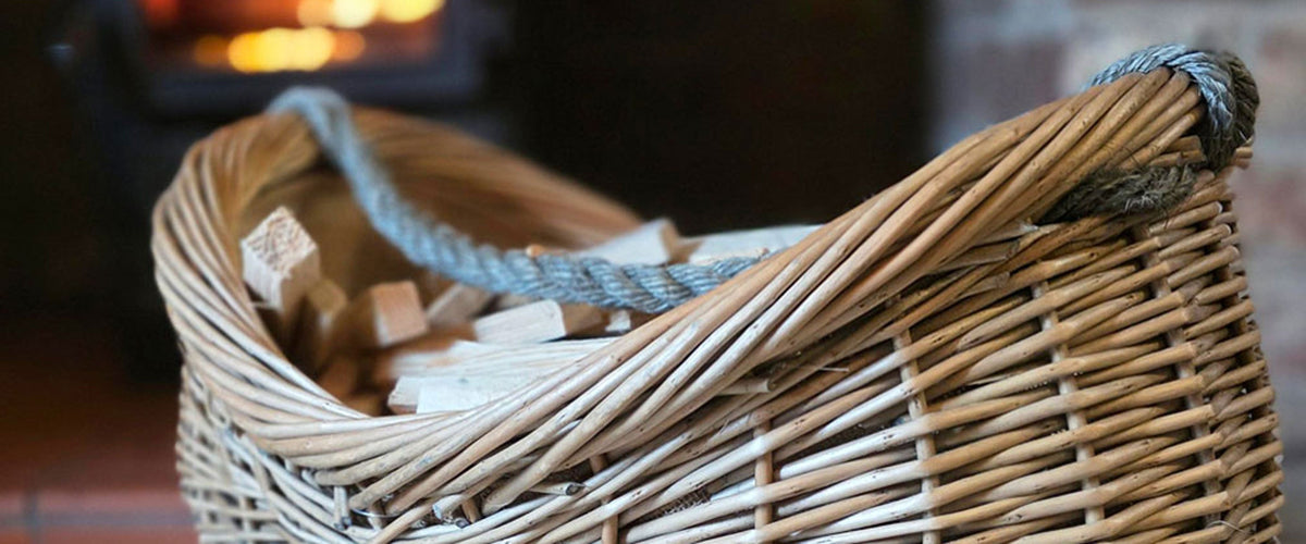 Curve topped wicker firewood basket filled with kindling sticks next to a lit wood burning stove.