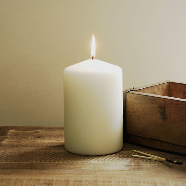 Lit 145 hour burn time church pillar candle on a wooden table next to a wooden box.