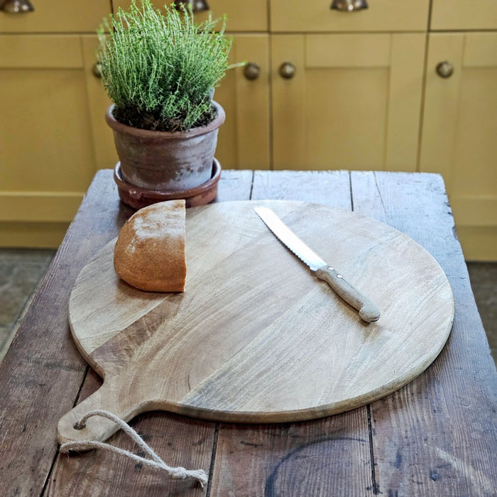 Large round wooden chopping board with bread and knife