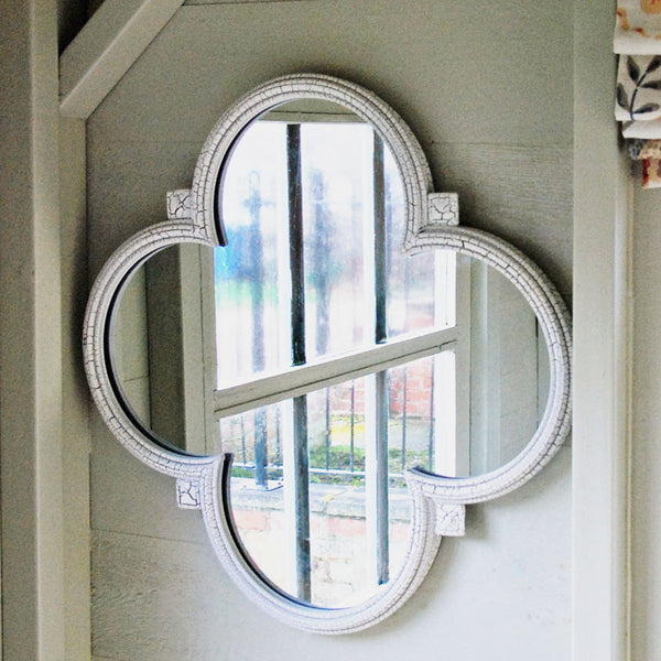 Small white white club shaped wall mirror mounted on a bedroom wall.