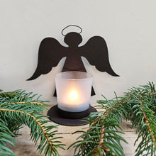 Iron angel silhouette with glass tea light holder surrounded by Christmas foliage.