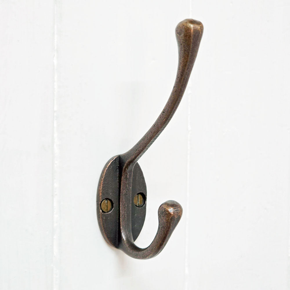 Antique copper metal coat hook mounted upon a white wooden panelled wall.
