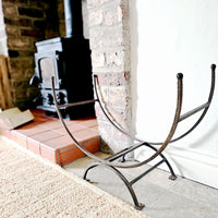 Iron firewood log holder next to wood burning stove.