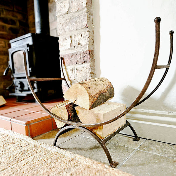 Wrought iron firewood holder with logs in front of a stone fireplace.