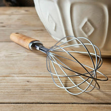 Balloon whisk on a kitchen table next to a ceramic mixing bowl