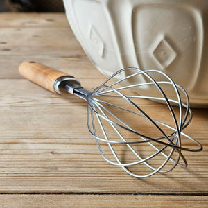 Balloon whisk on a kitchen table next to a ceramic mixing bowl