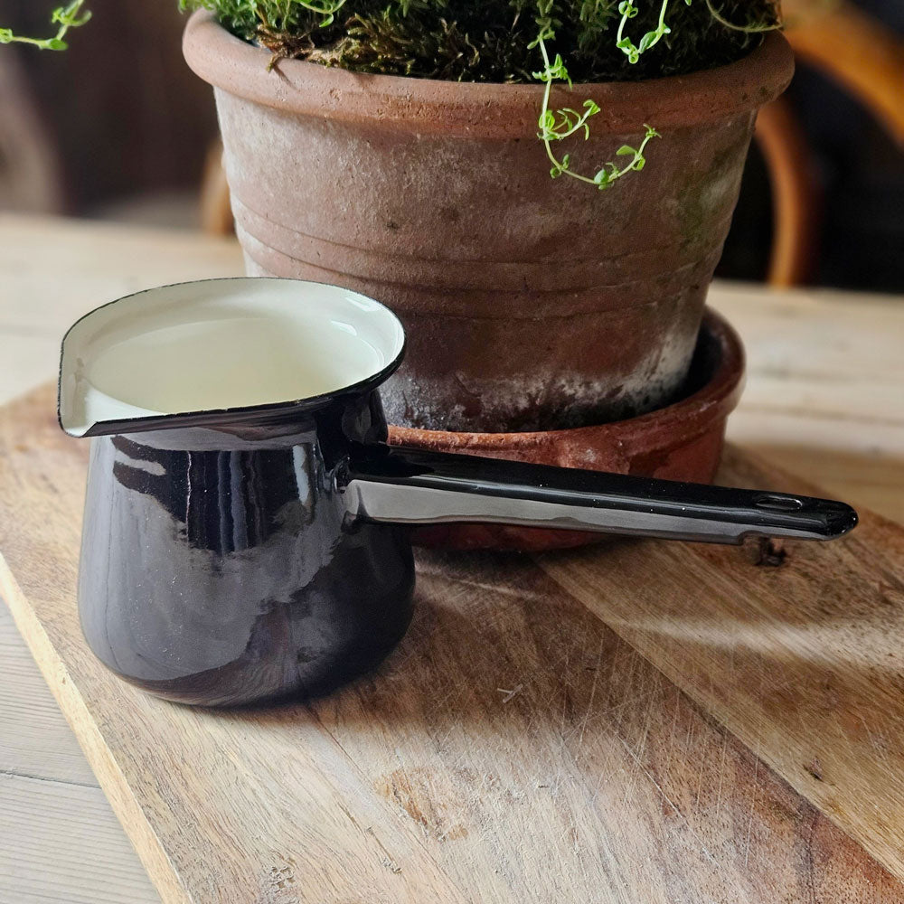 Black enamel pan with white enamel lining on a wooden board next to a pot of fresh Thyme.