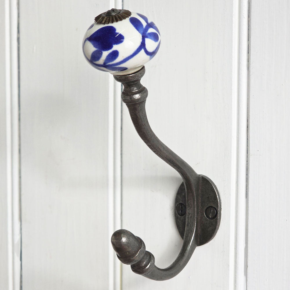 A dark metal coat rack hook with a white ceramic knob featuring a blue floral pattern, mounted on a white paneled door.