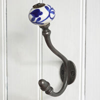A dark metal coat rack hook with a white ceramic knob featuring a blue floral pattern, mounted on a white paneled door.