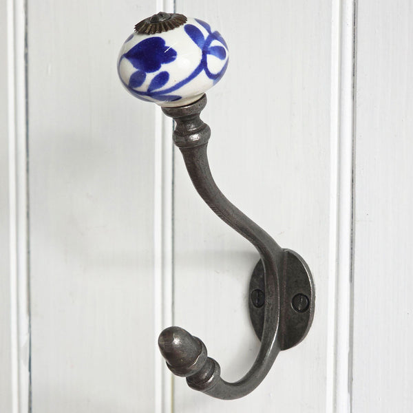 A dark metal coat rack hook with a white ceramic knob featuring a blue floral pattern, mounted on a white paneled door.