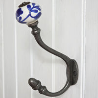 A rustic metal hook with a white ceramic knob featuring a blue floral pattern, mounted on a white paneled door.