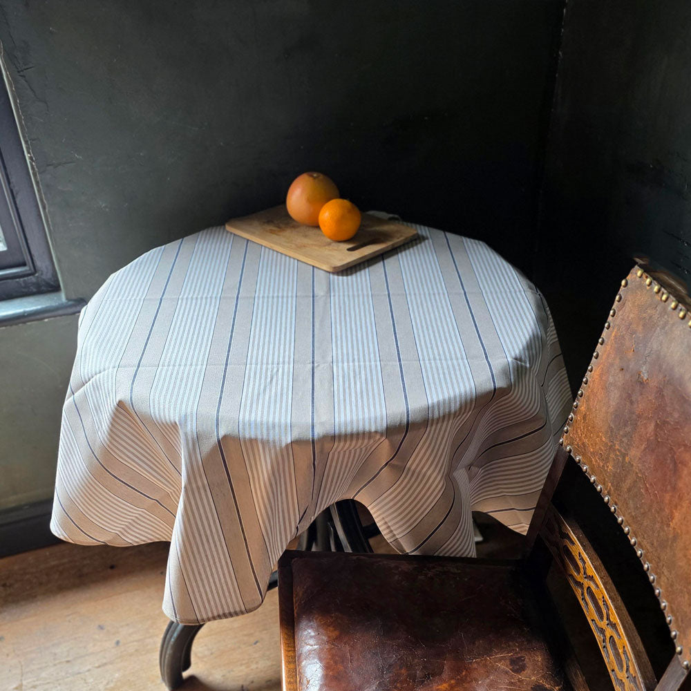 Round table with a striped tablecloth and oranges on a wooden floor.
