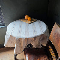 Round table with a striped tablecloth and oranges on a wooden floor.