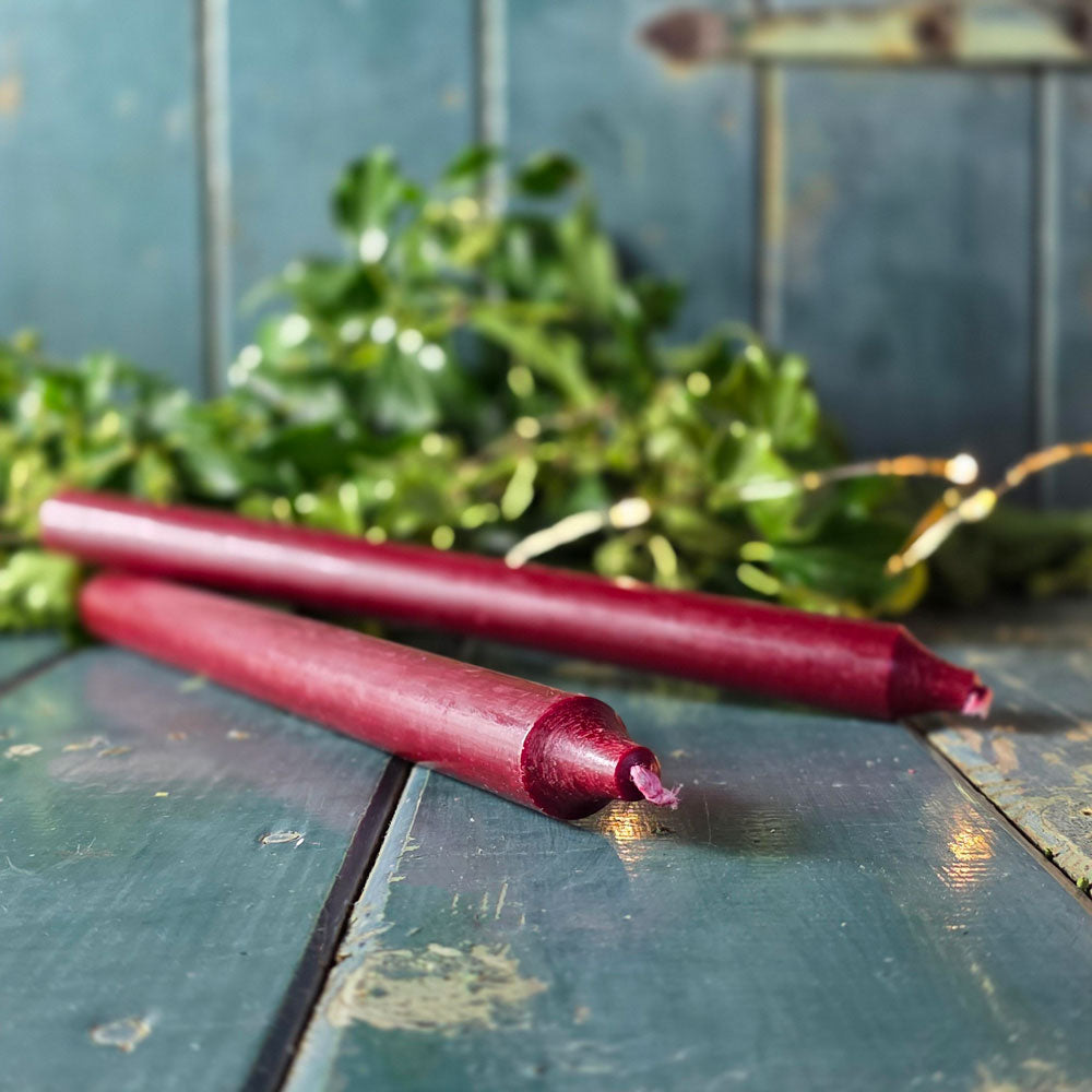 Dark red long Christmas dinner candle against Christmas foliage.