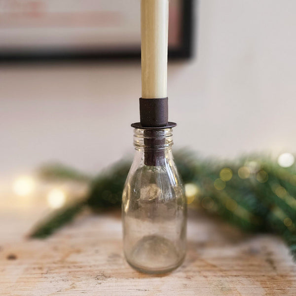 Clear glass bottle with a candle inside on a wooden surface with blurred greenery in the background