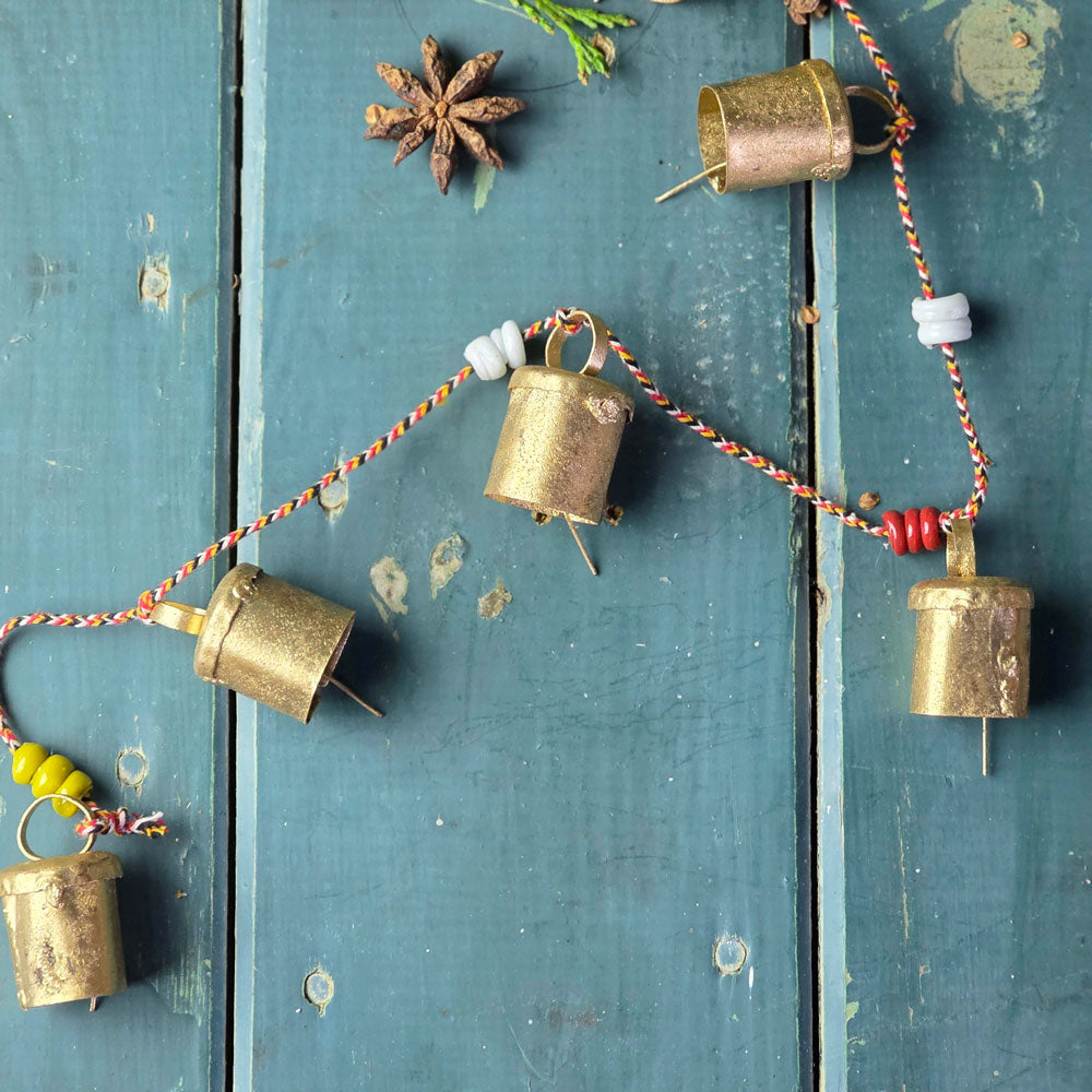 Decorative string of brass bells with colorful beads on a rustic wooden surface.