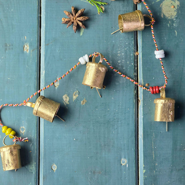 Decorative string of brass bells with colorful beads on a rustic wooden surface.