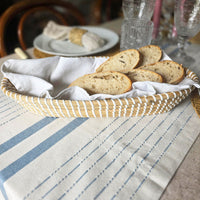 Bread slices in a woven basket on a striped tablecloth with glasses in the background