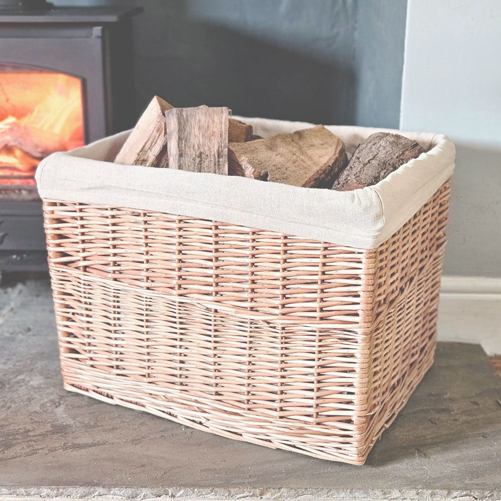 Bruton lined wicker log basket filled with logs next to a lit wood burning stove