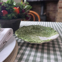A green and white ceramic bowl with a textured leaf design, styled on a green and white checkered tablecloth next to a folded white napkin.