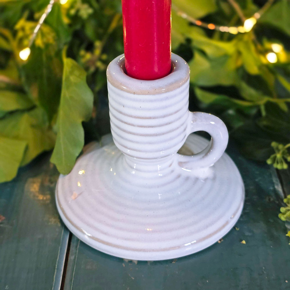 White ceramic candle holder with a red candle against a green leafy background