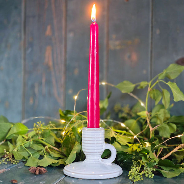 Red candle in a white holder surrounded by greenery on a rustic wooden surface