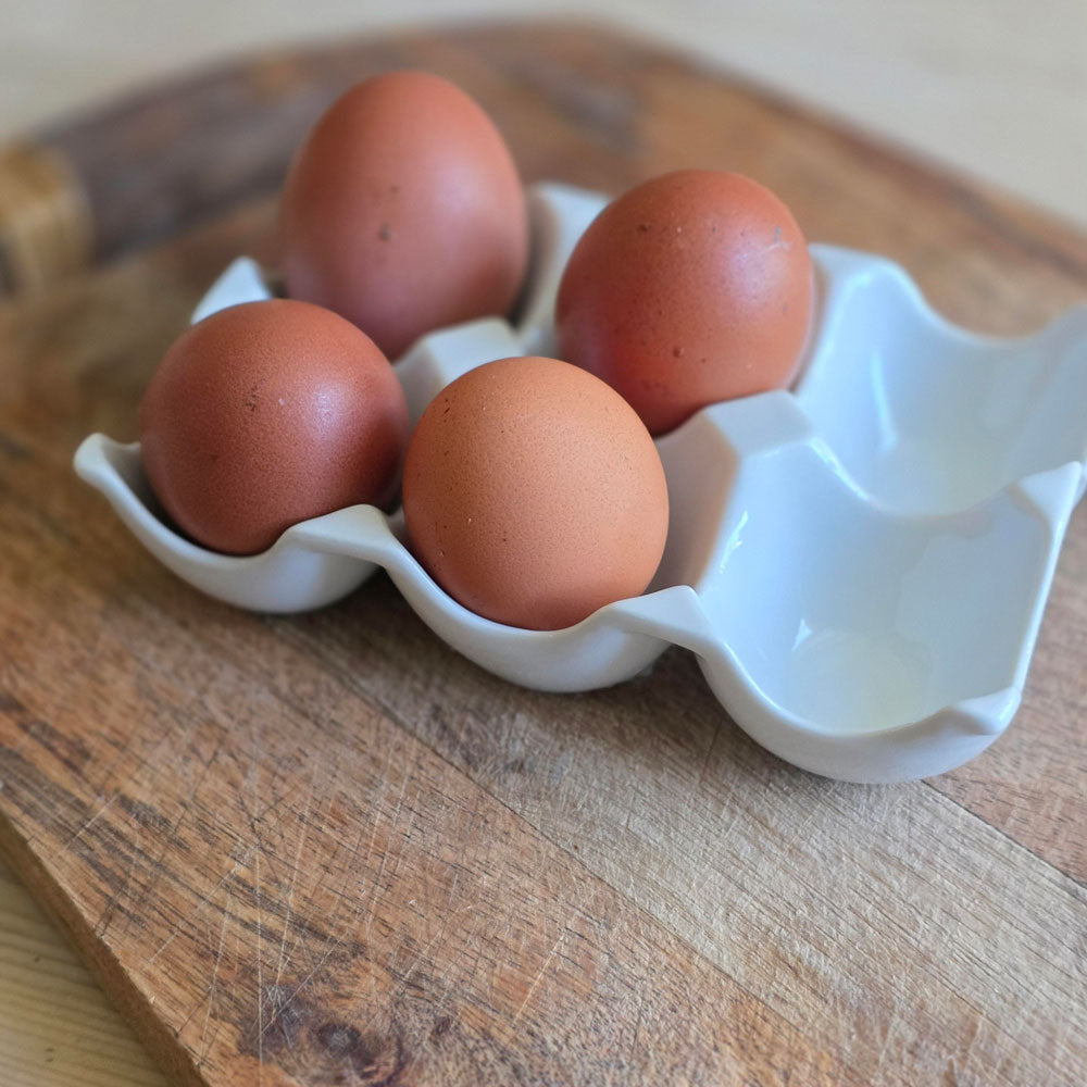 Four brown eggs in a white ceramic egg holder on a wooden surface