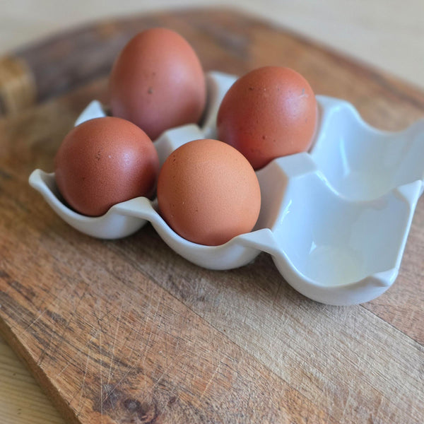 Four brown eggs in a white ceramic egg holder on a wooden surface