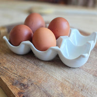 Four brown eggs in a white ceramic egg holder on a wooden surface