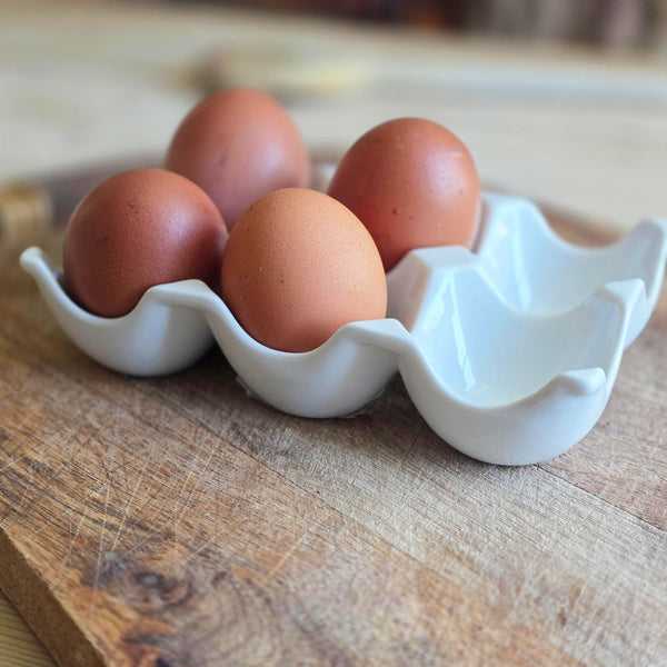 Four brown eggs in a white ceramic egg holder on a wooden surface