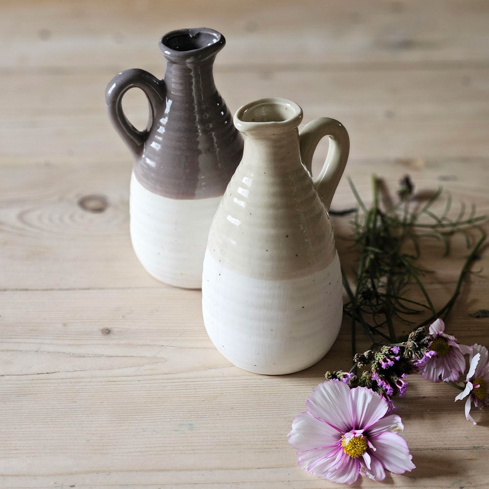 Small Earthenware flower vase jugs on a kitchen table with flower stems.