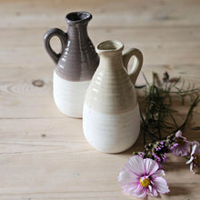 Small Earthenware flower vase jugs on a kitchen table with flower stems.