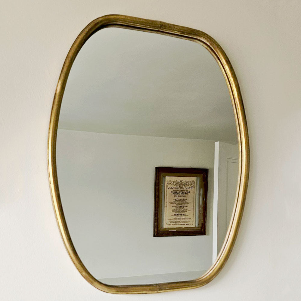 Gold-framed mirror on a white wall with a framed document reflected in it.