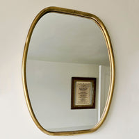 Gold-framed mirror on a white wall with a framed document reflected in it.