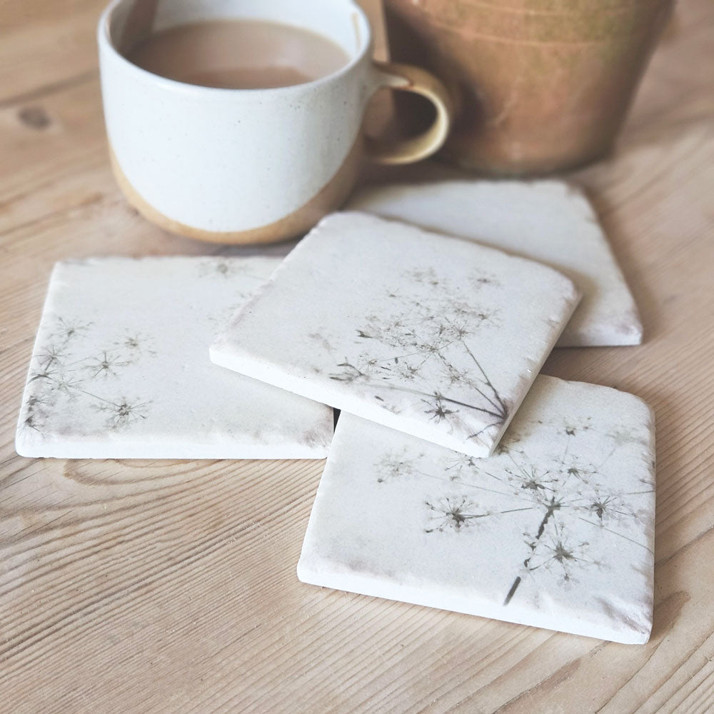 Four cow parsley coasters on a kitchen table next to coffee cup on a table.