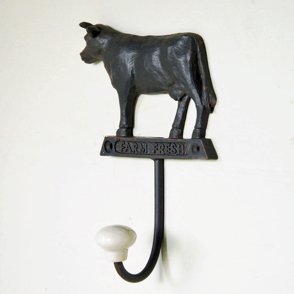 Cast metal cow wall hook with ceramic tip against cream background