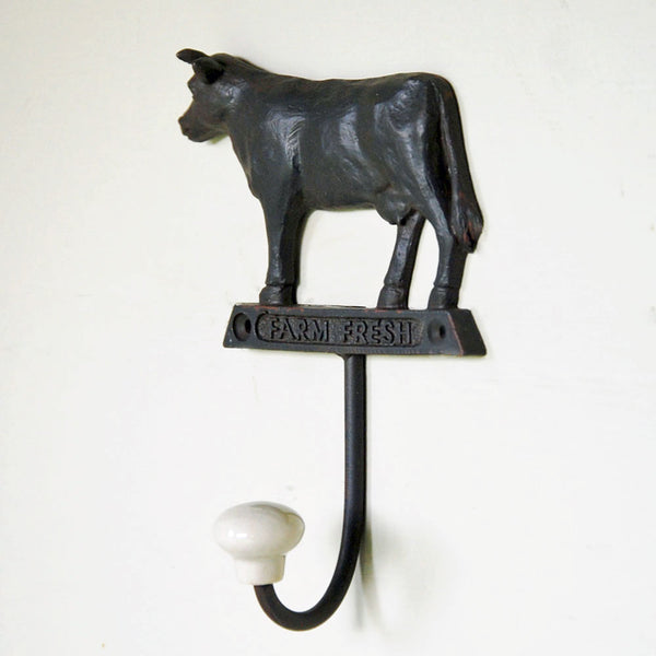 Cast metal cow wall hook with ceramic tip against cream background