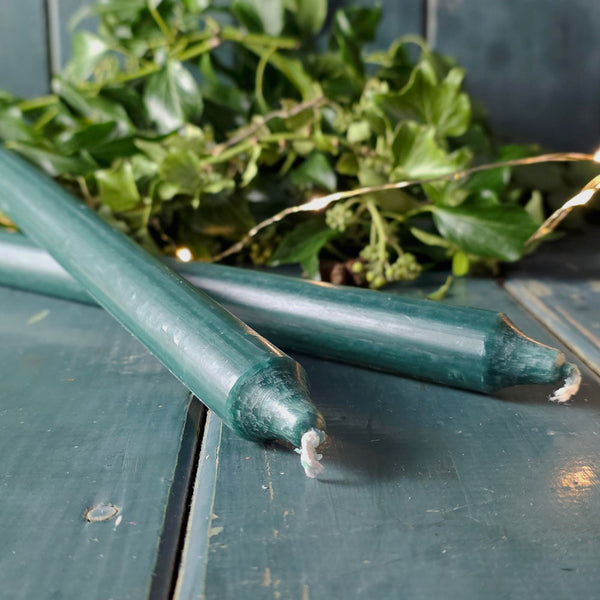 Dark green Danish dinner candles on a table with foliage and Christmas lights.