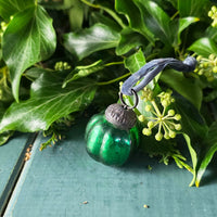 Green glass Christmas tree decoration. with metal top on a green leafy background