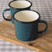 Pair green enamel mugs on a wooden board on a natural checked tablecloth.