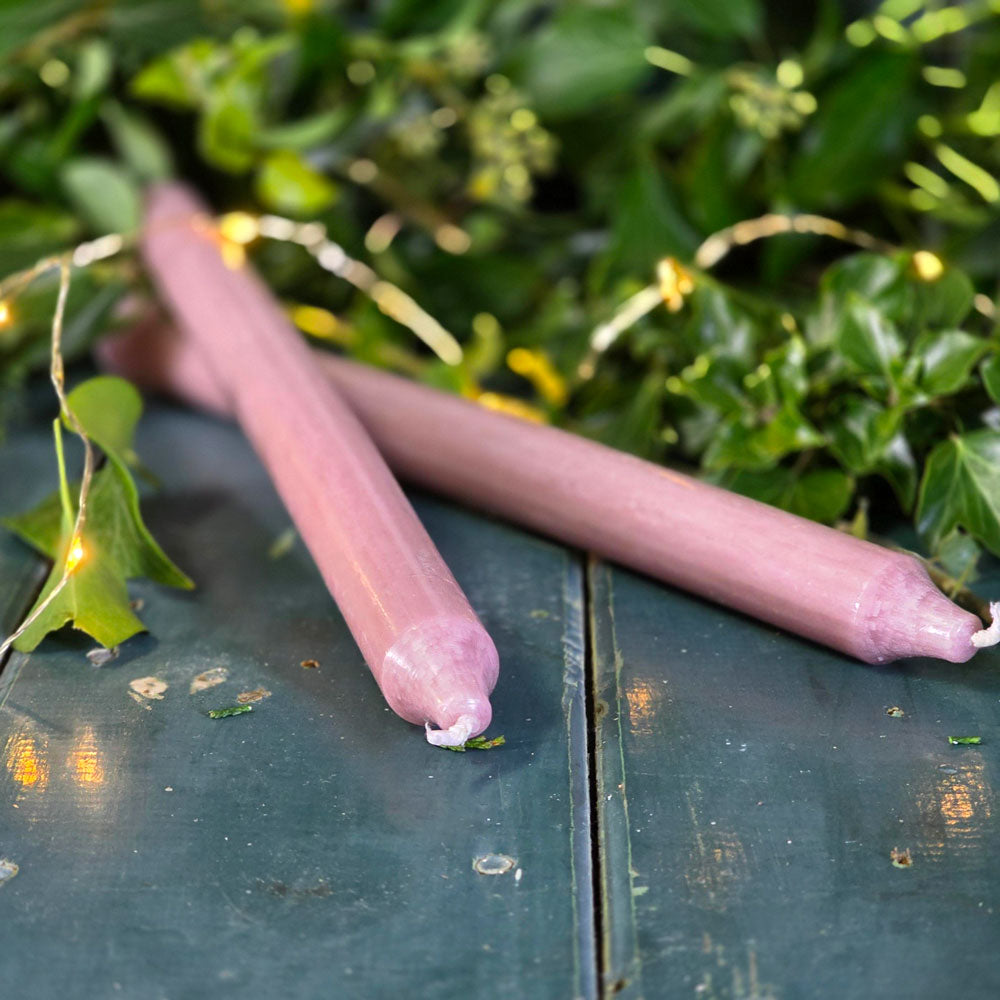 Two pink candles on a textured surface with green foliage in the background