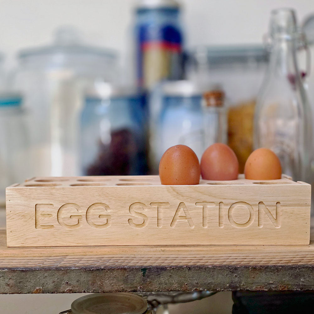 Wooden egg holder labeled 'Egg Station' with eggs on a kitchen counter.