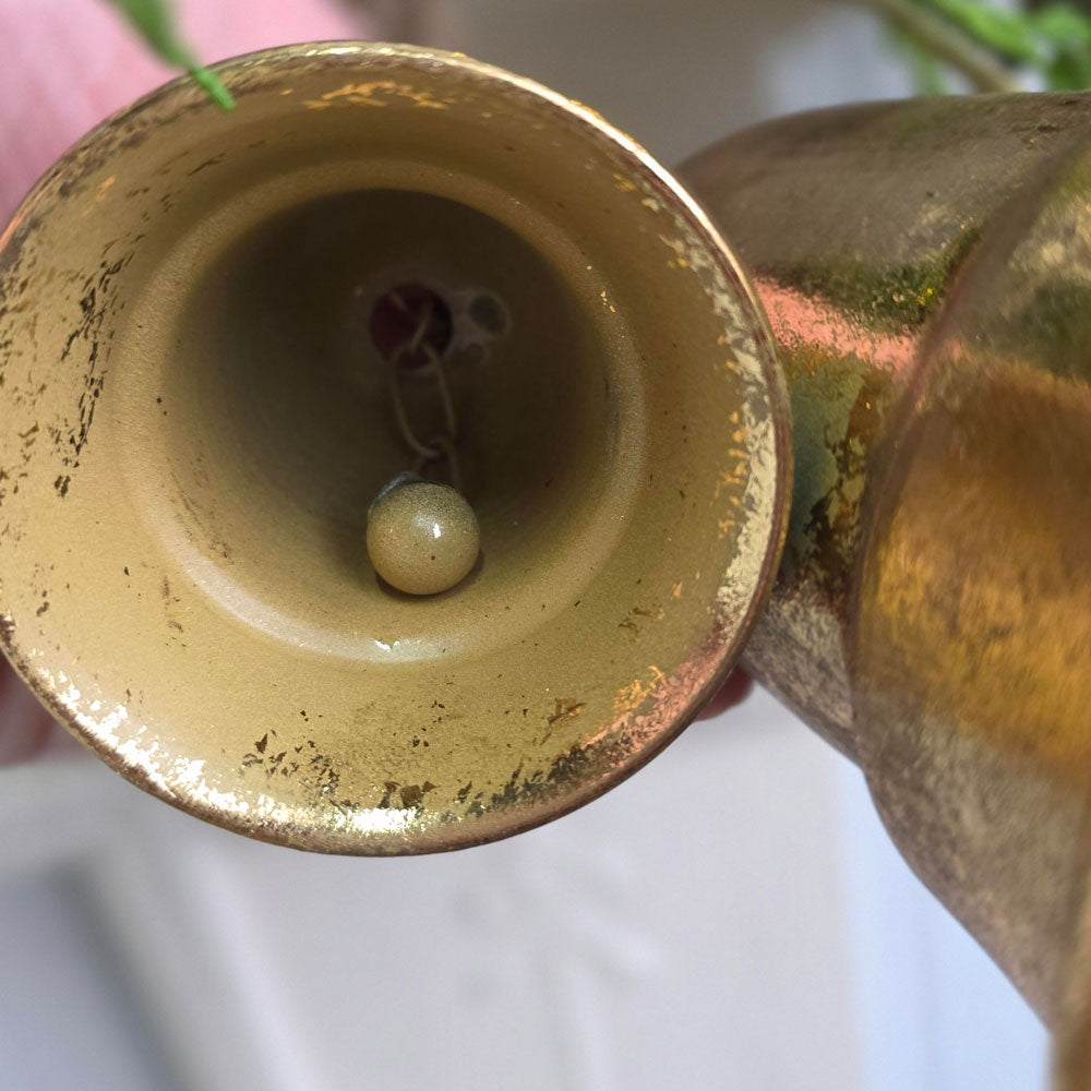 Close-up of a brass bell-shaped vessel or horn showing the interior with a small bead inside, featuring a distressed gold finish.