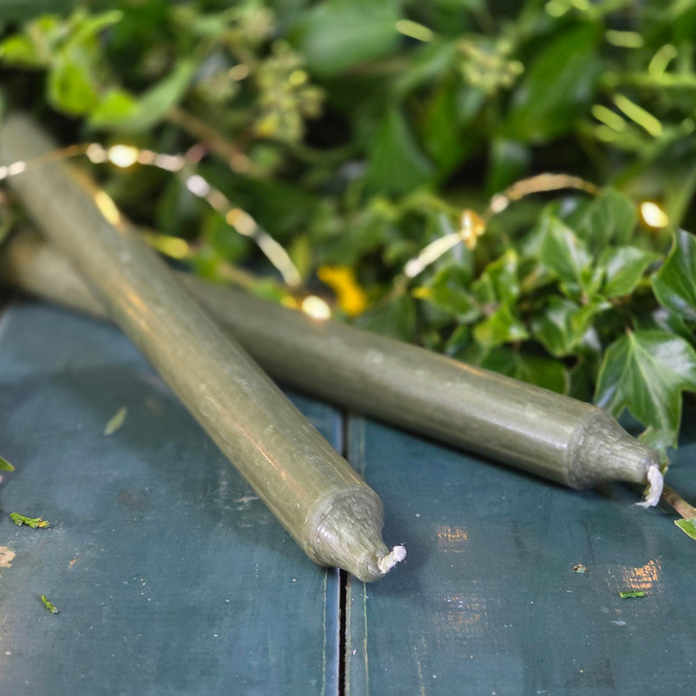 Two green Danish dinner candles surrounded by foliage.