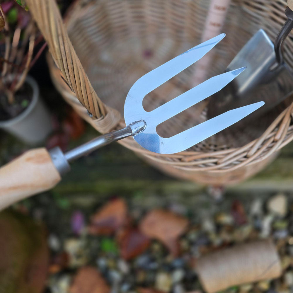 Metal garden fork with wooden handle in front of a wicker basket on a blurred garden background