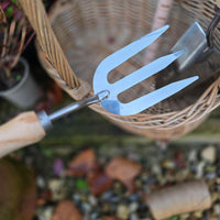 Metal garden fork with wooden handle in front of a wicker basket on a blurred garden background