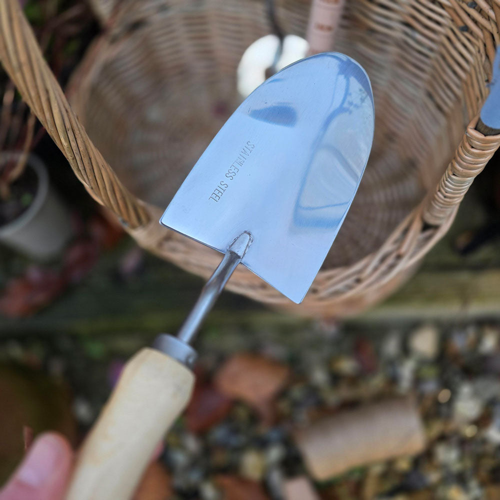 Gardening trowel with a decorative blade held in front of a wicker basket.