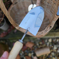 Gardening trowel with a decorative blade held in front of a wicker basket.