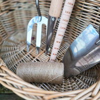 Gardening tools including a fork, trowel, and measuring tool on a wicker surface.